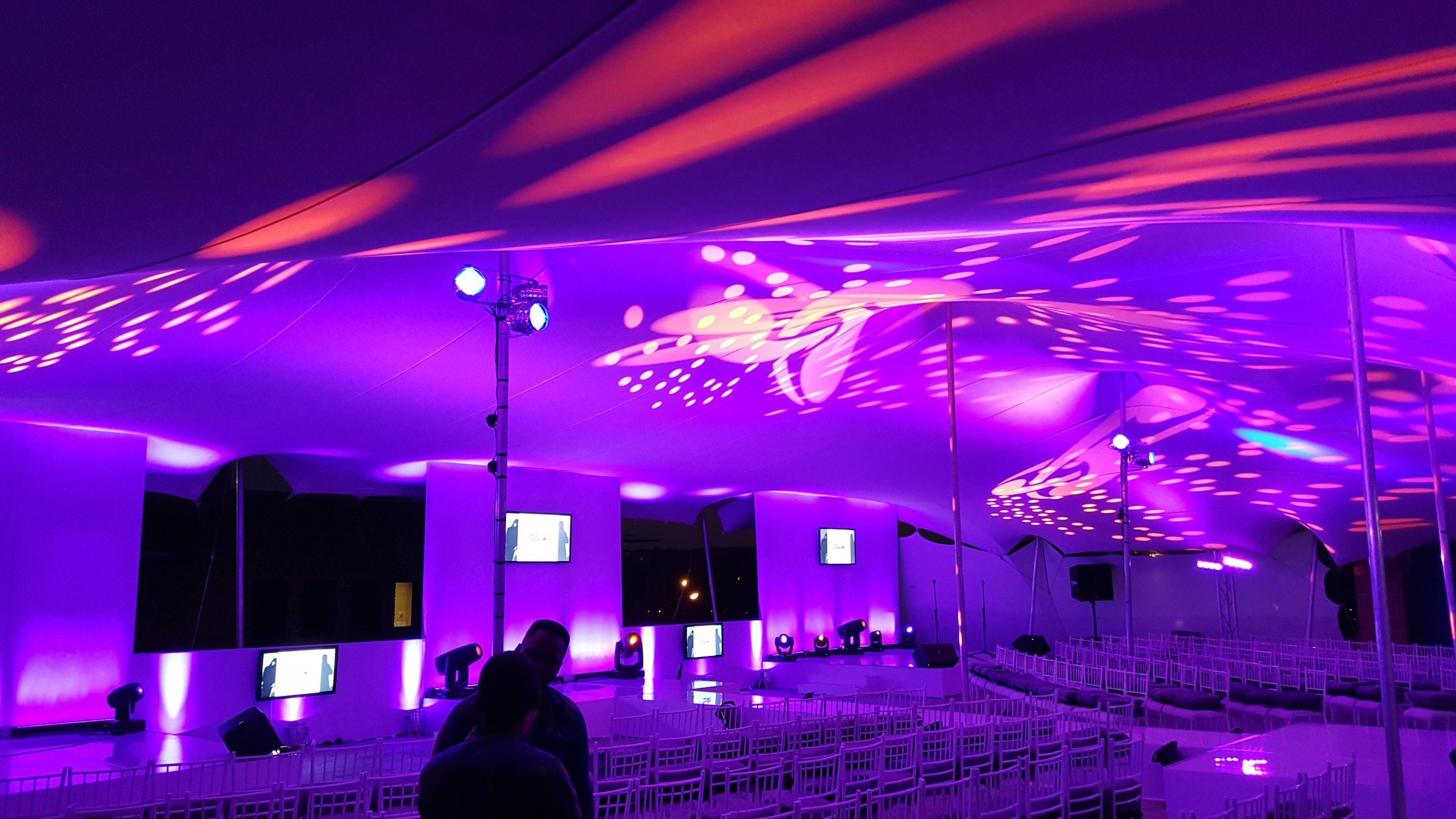 Stretch tent interior under a magenta wash with fashion screens and Chiavari seating