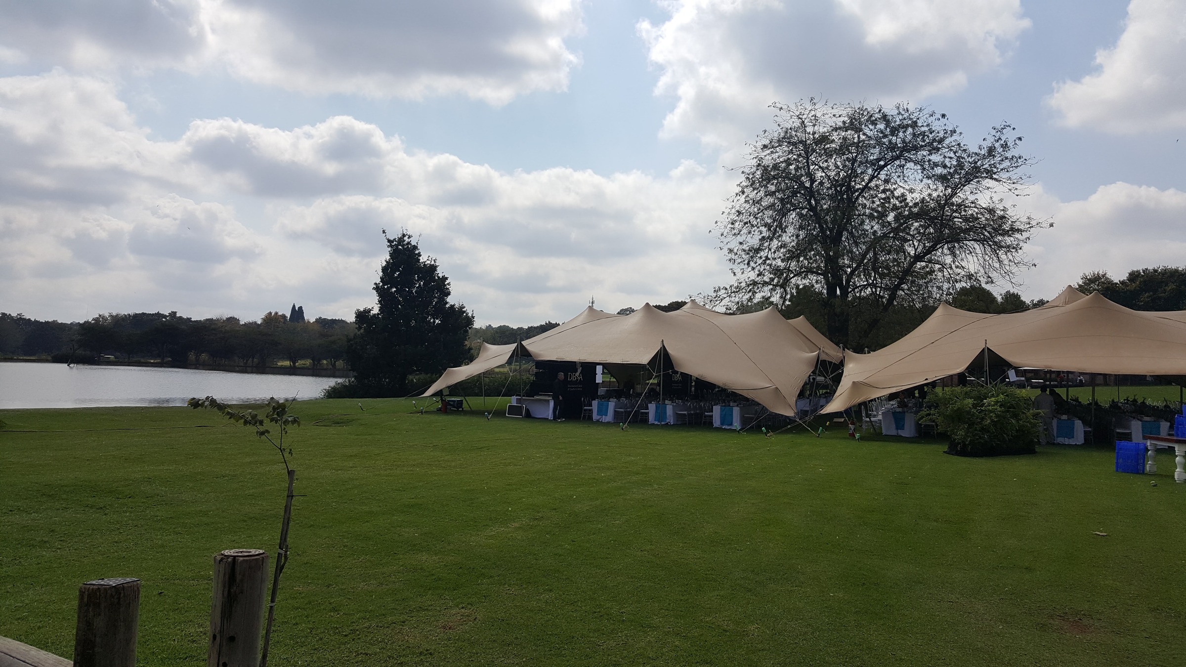 Exterior view of tan stretch tents on a lake lawn with a DBSA backdrop and white banquet tables under blue-trimmed table linen