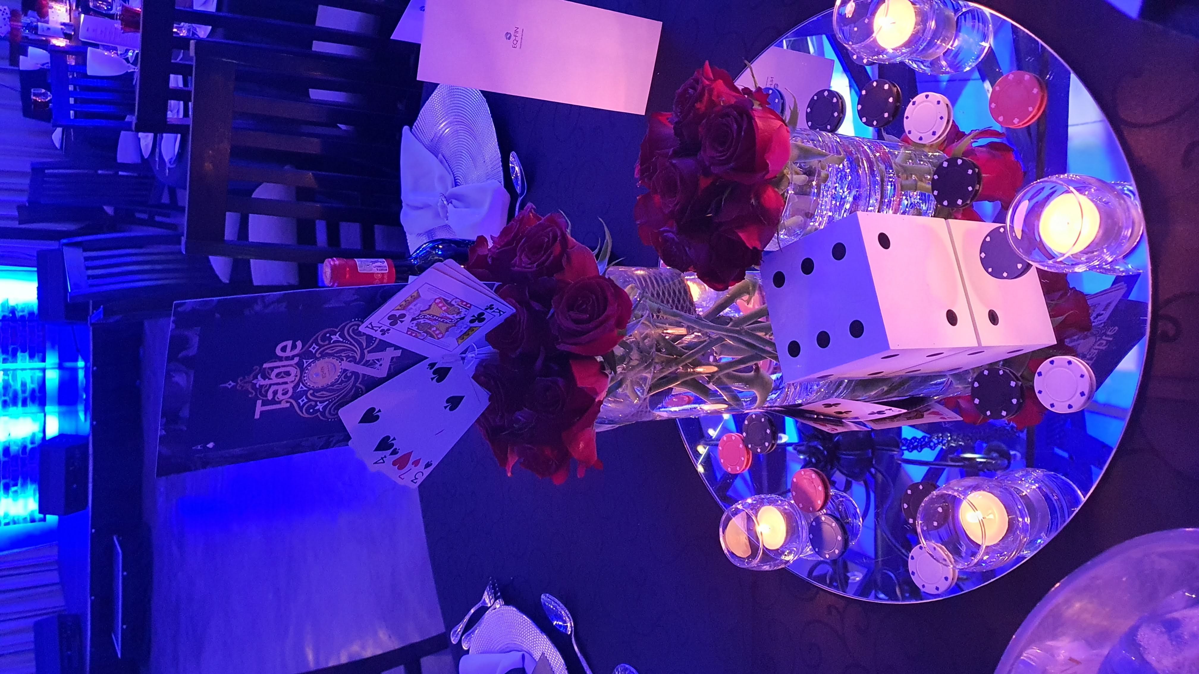 Gala table with an EQ-FIN menu card, playing cards, red roses, dice, and poker chips on a mirrored plate