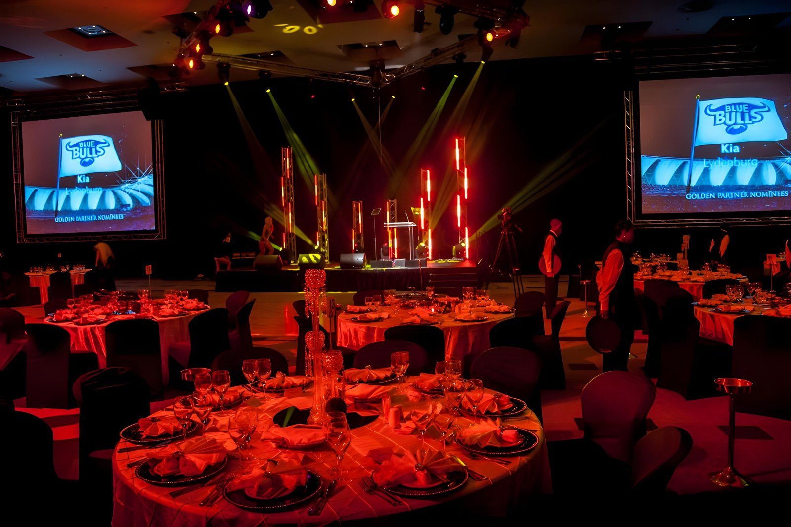 Banquet floor with Blue Bulls / Kia Lydenburg GOLDEN PARTNER NOMINEES on dual screens under a red and yellow stage wash