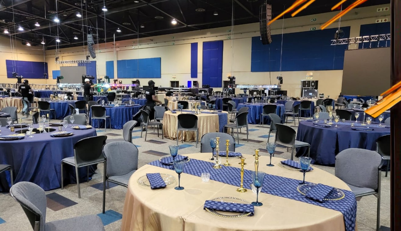 Banquet hall setup with navy and gold linens, gold candelabra, blue glassware, and overhead truss