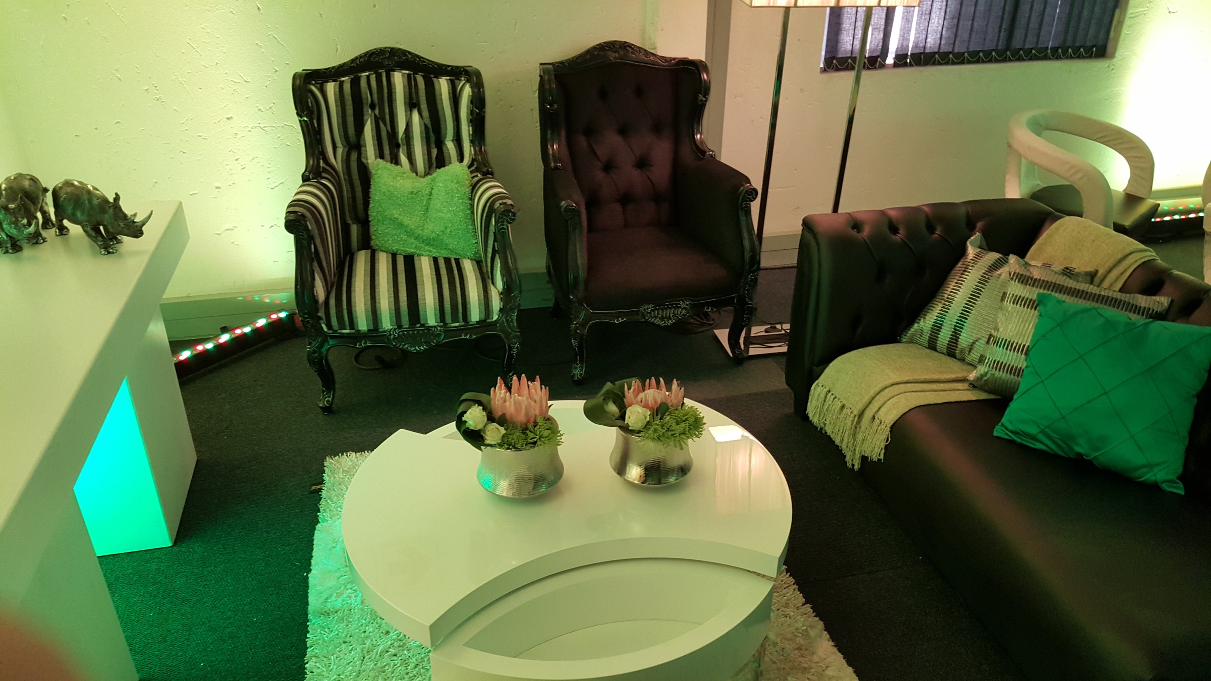 Lounge corner with pink proteas, a Chesterfield sofa and wingback chairs under a green wash, with rhino sculptures