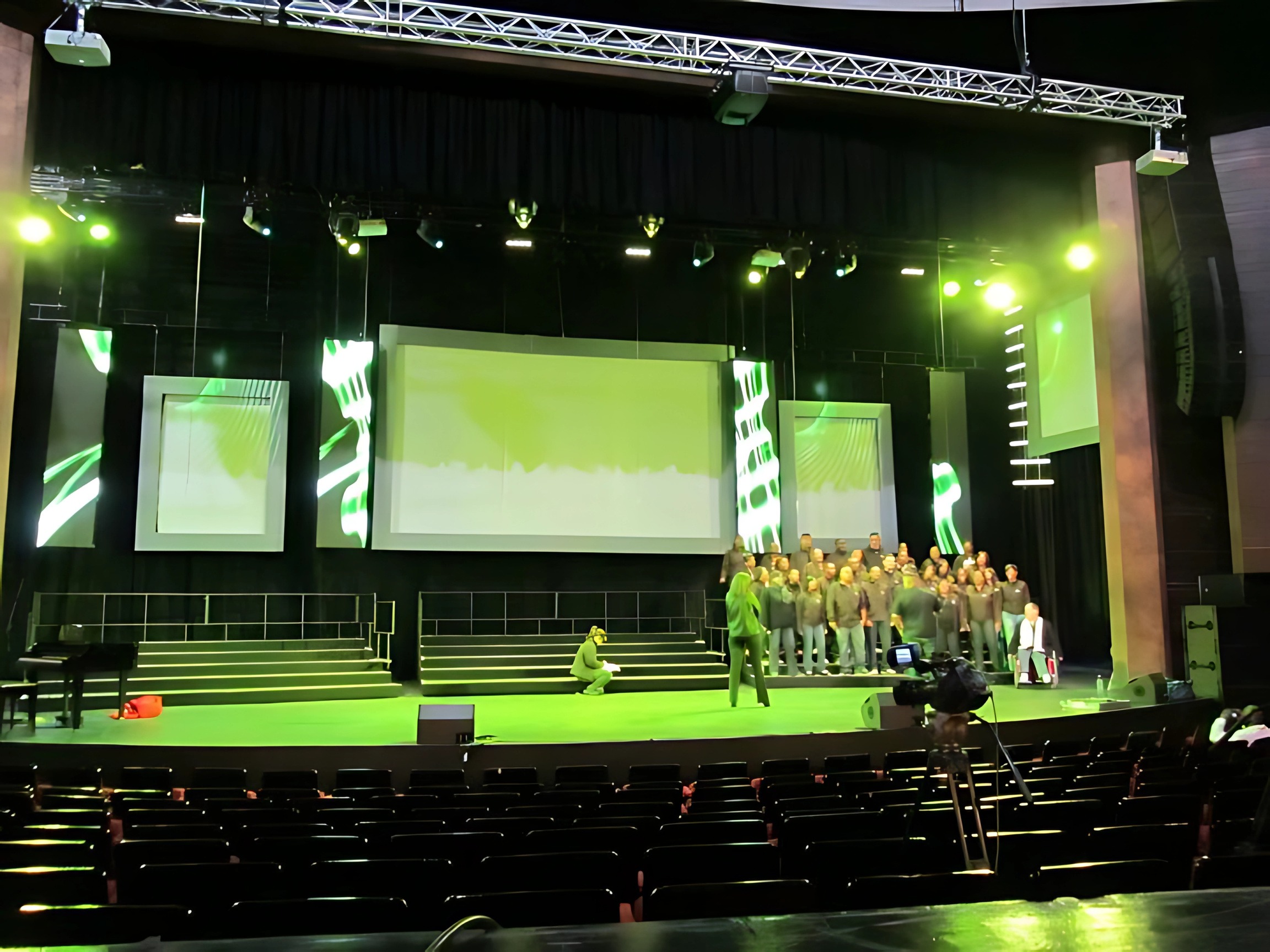 Choir on stage between green LED screens with a camera on the floor