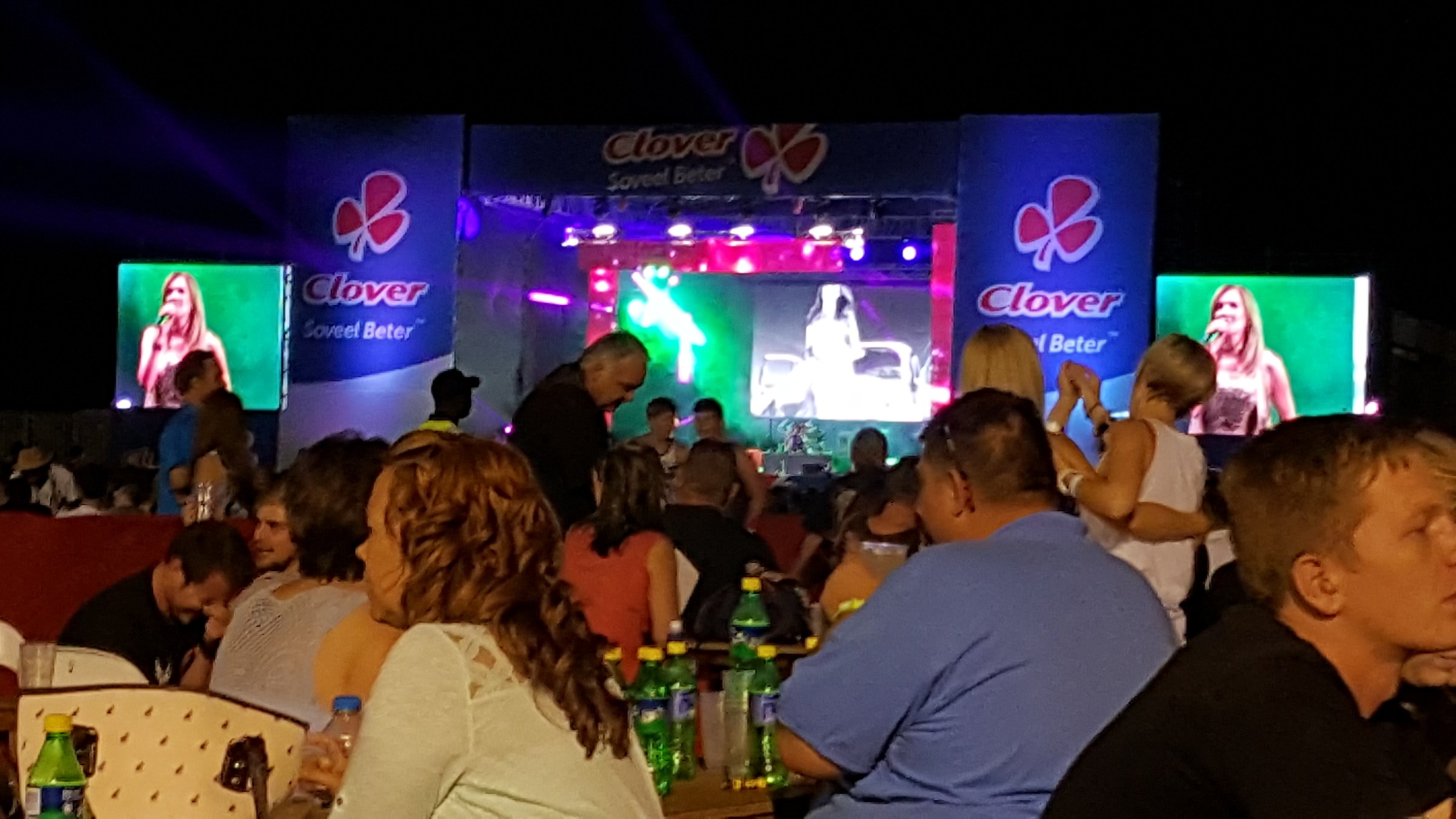 Night stage with a performer on LED screens framed by Clover banners