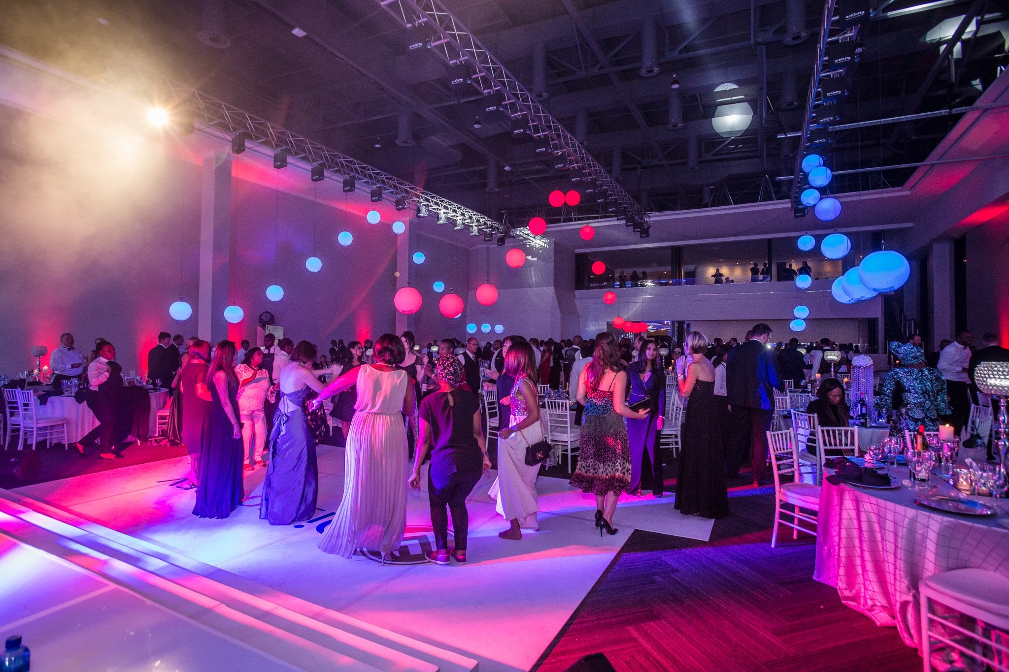 Dance floor with the large IIG circular floor logo, pink and blue globe lanterns, and formal guests