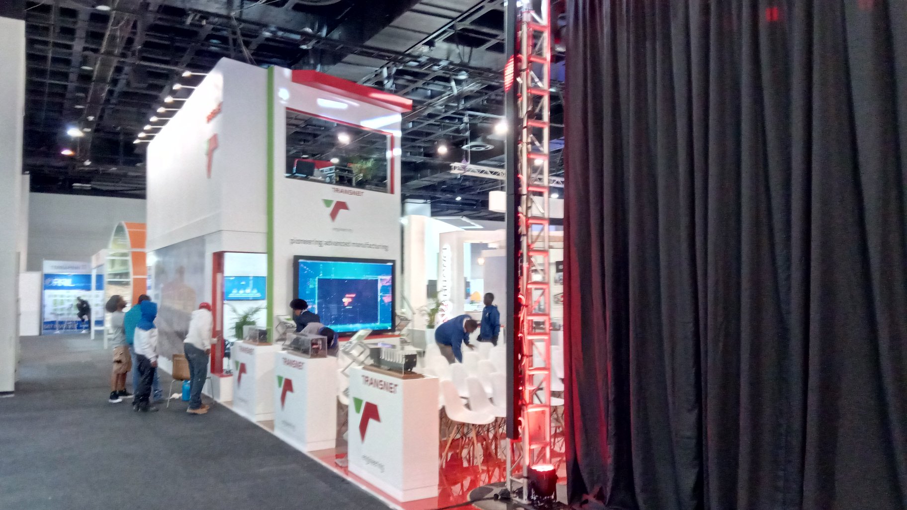 Two-storey white expo stand with the TRANSNET logo and pioneering advanced manufacturing messaging on a glossy red floor