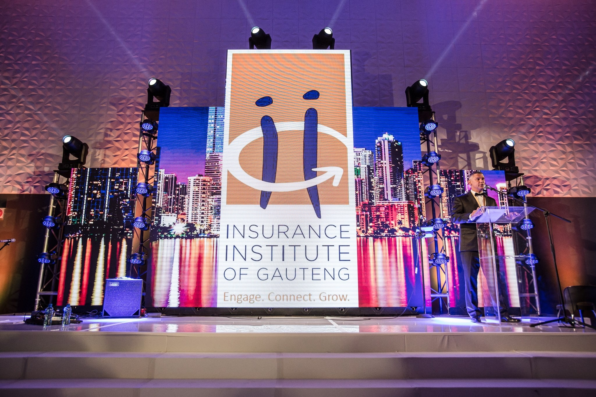 Stage with Insurance Institute of Gauteng LED, city skyline side panels, and an acrylic lectern