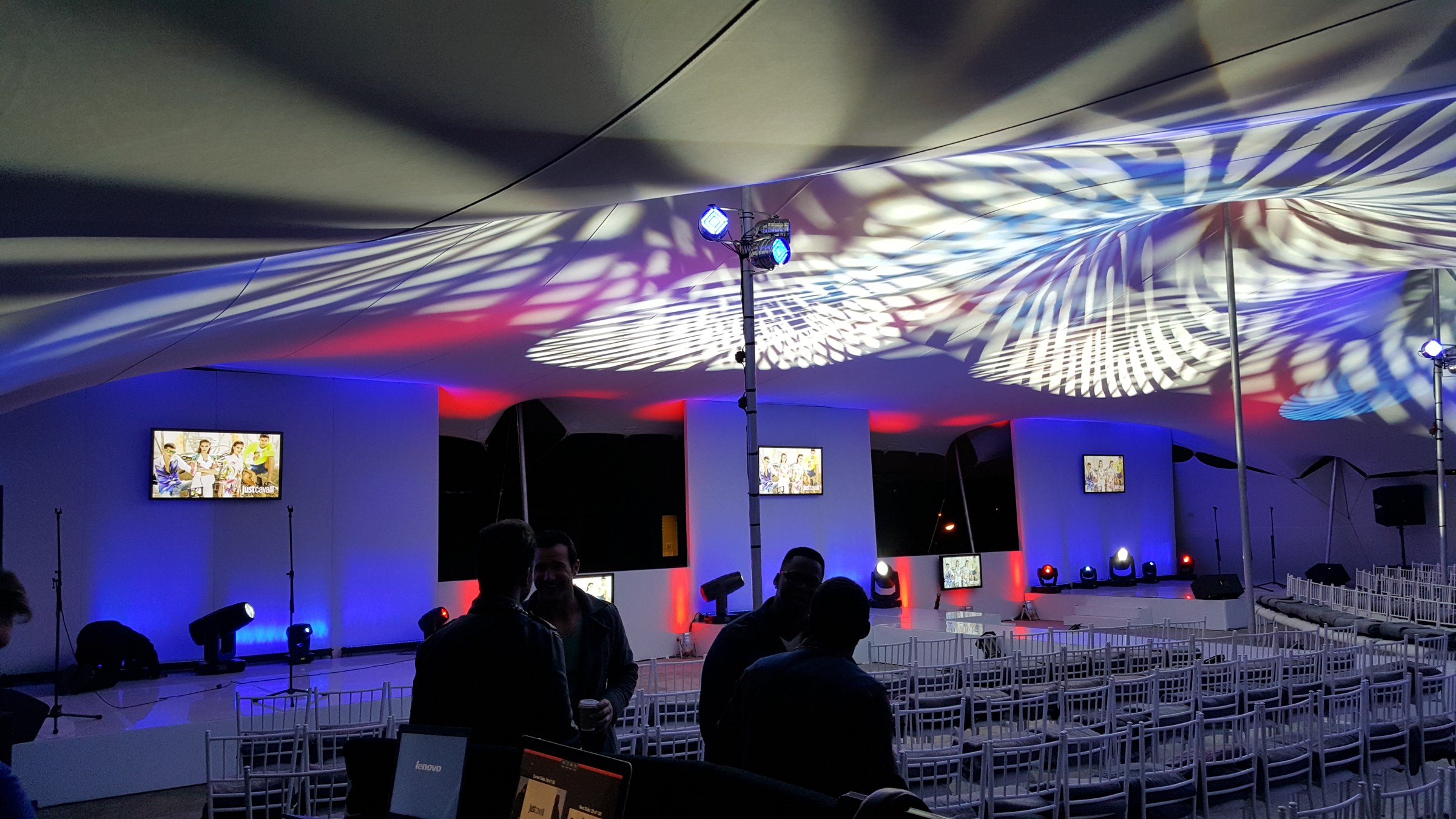 Stretch tent interior with projected colour patterns on the ceiling, blue and red wall washes, and fashion screens