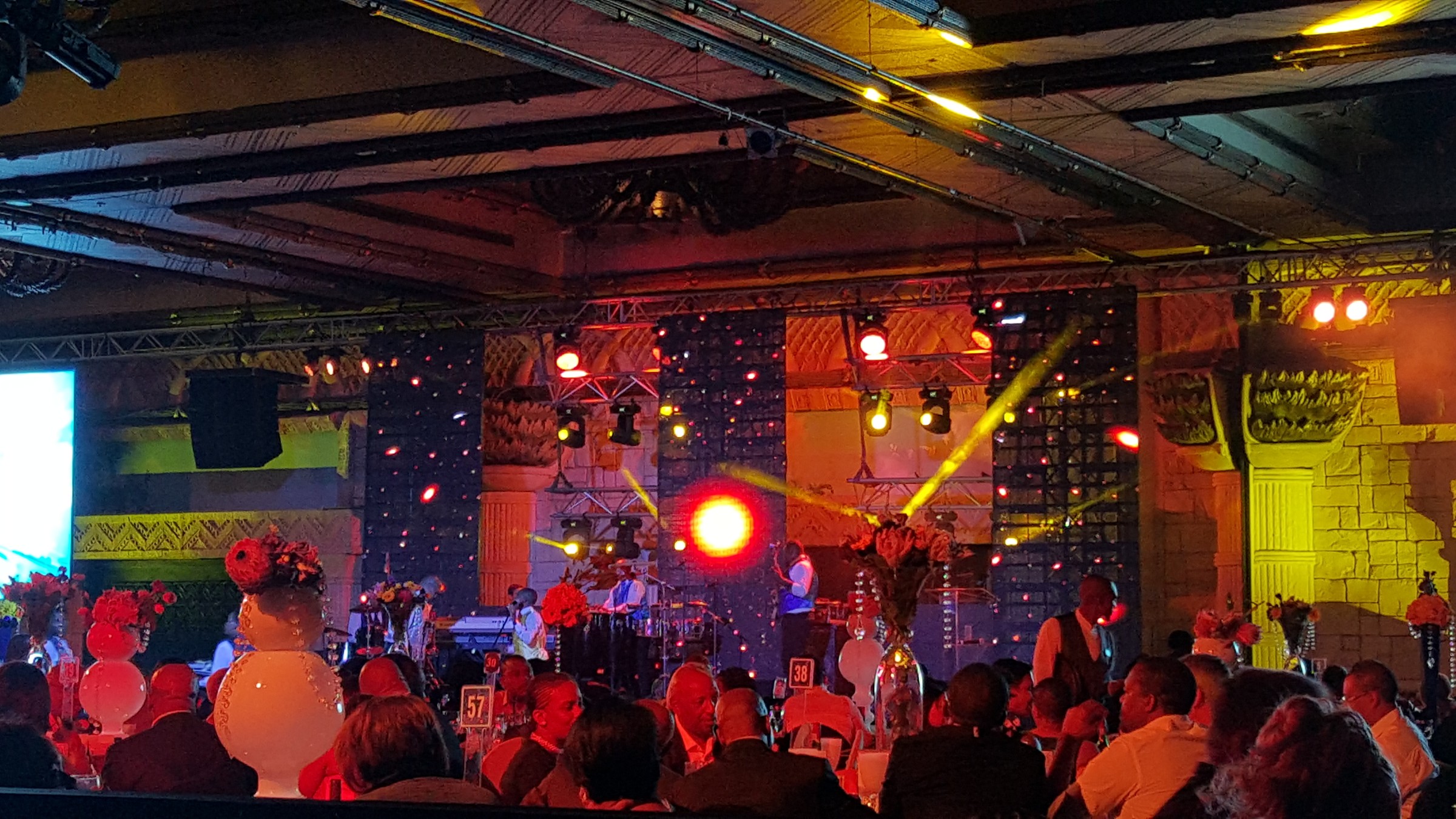 Live band on a stage under coloured beams, with a side screen visible