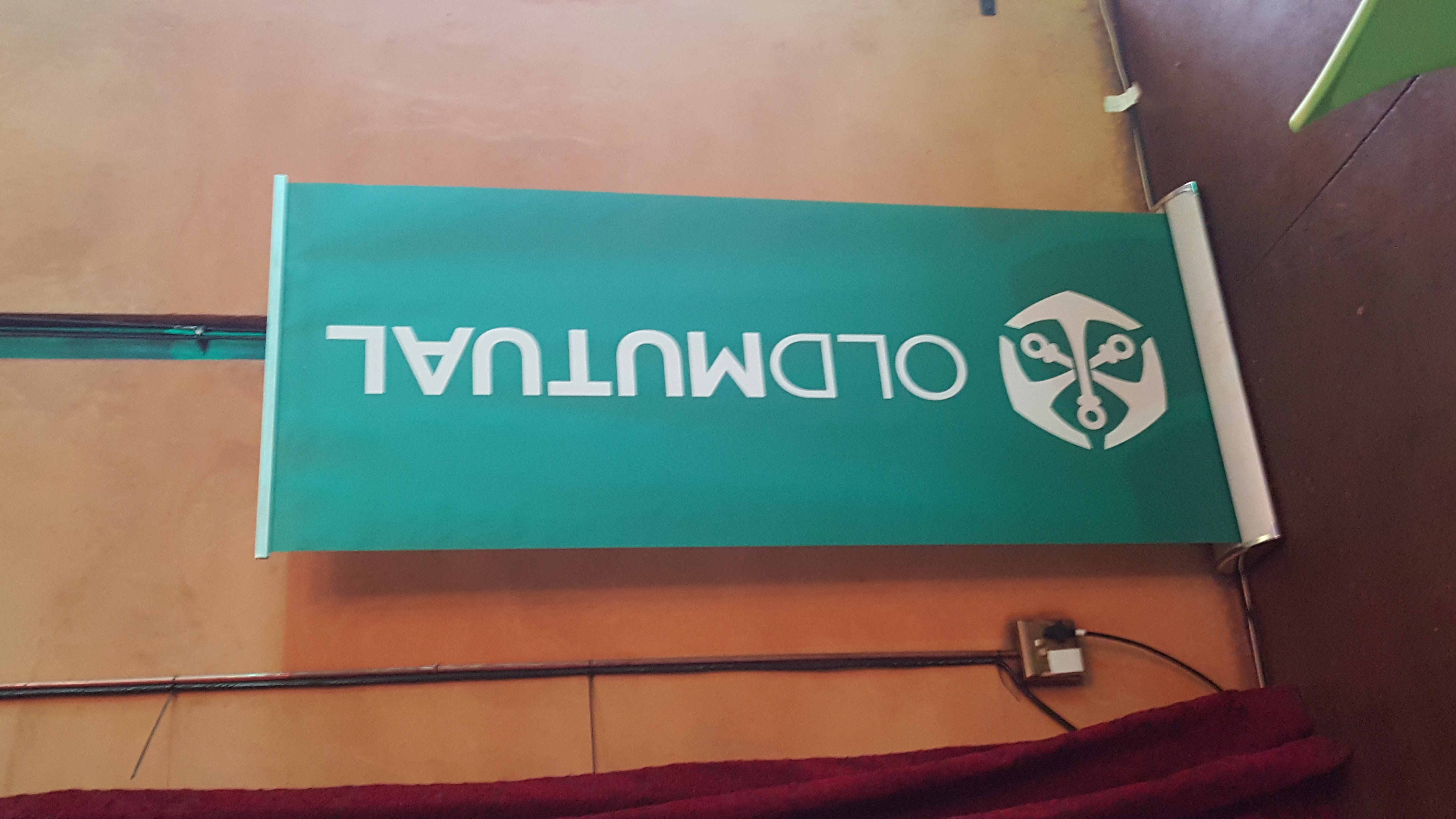 Teal OLD MUTUAL pull-up banner against a textured wall with a red cloth edge below